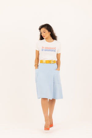 Raven haired women in a Le weekend graphic tee and a baby blue skirt looking sideways.