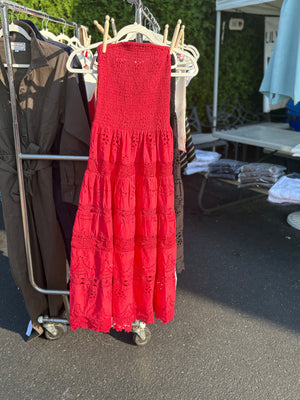 Strapless eyelet midi dress in watermelon with clothes pins attaching it to a hanger on a rack.