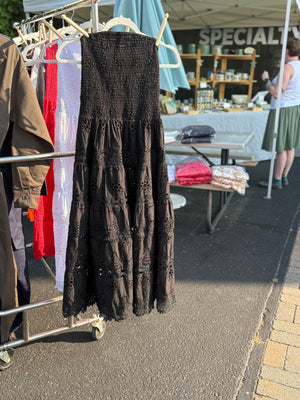 Strapless eyelet midi dress in black with clothes pins attaching it to a hanger on a rack.