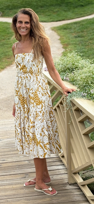 Woman in a floral strappy dress with pockets standing on a wooden bridge with greenery in the background