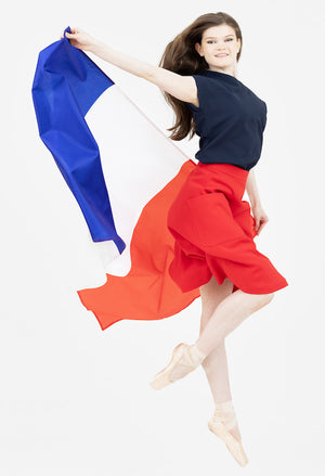 Ballerina in a navy Julie top and red midi skirt from Le Mireille Marche, leaping gracefully while holding a French flag.