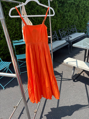 Orange strappy dress on a hanger blowing in the breeze with a blurred background