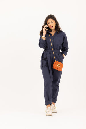 Young woman on a cell phone in a navy jumpsuit with sneakers.