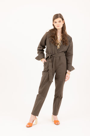 Young woman wearing an olive green jumpsuit styled with a gold chain necklace and orange heels.