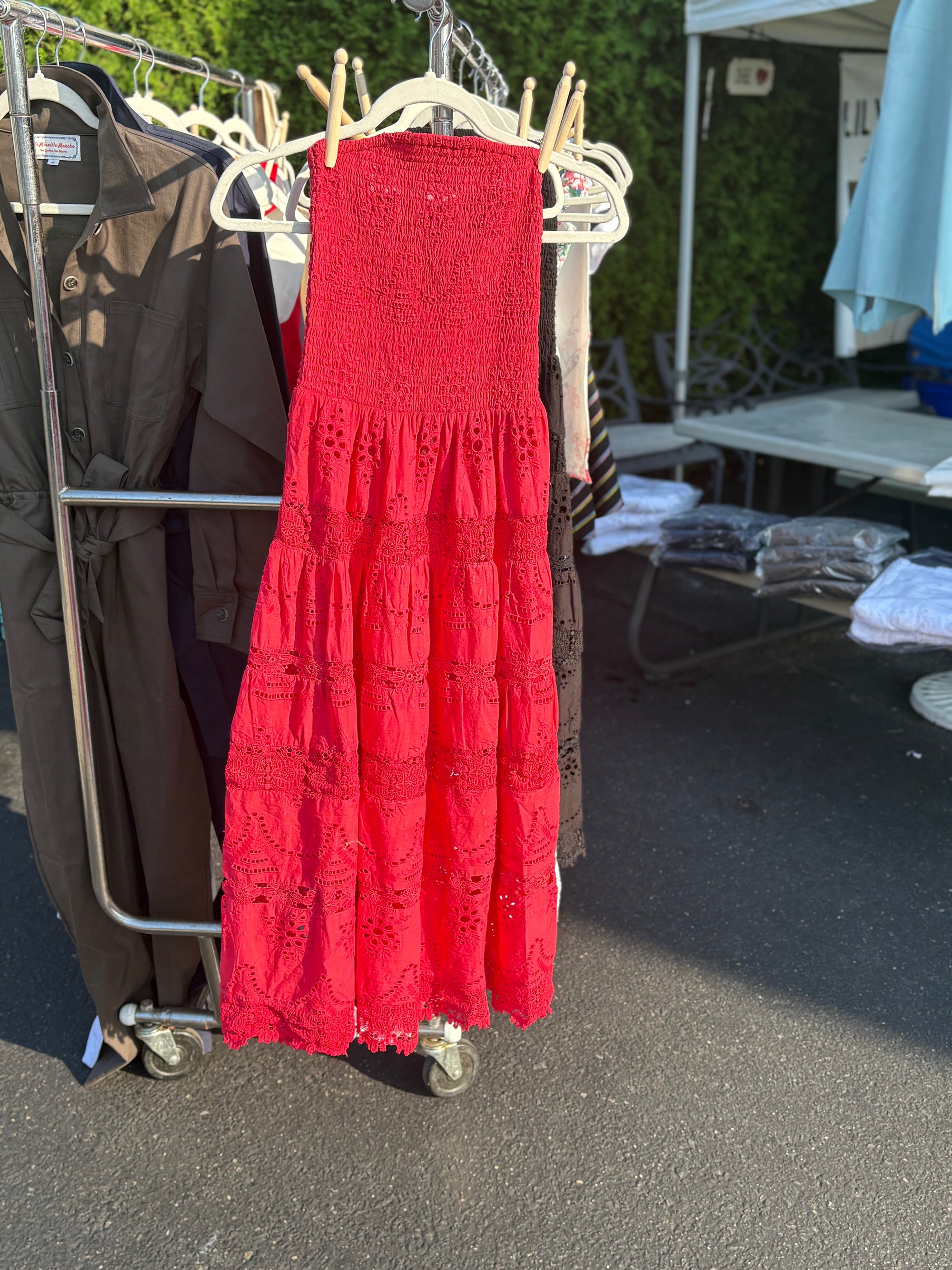 Strapless eyelet midi dress in watermelon with clothes pins attaching it to a hanger on a rack.