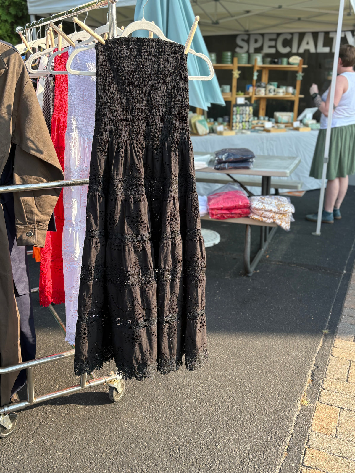 Strapless eyelet midi dress in black with clothes pins attaching it to a hanger on a rack.