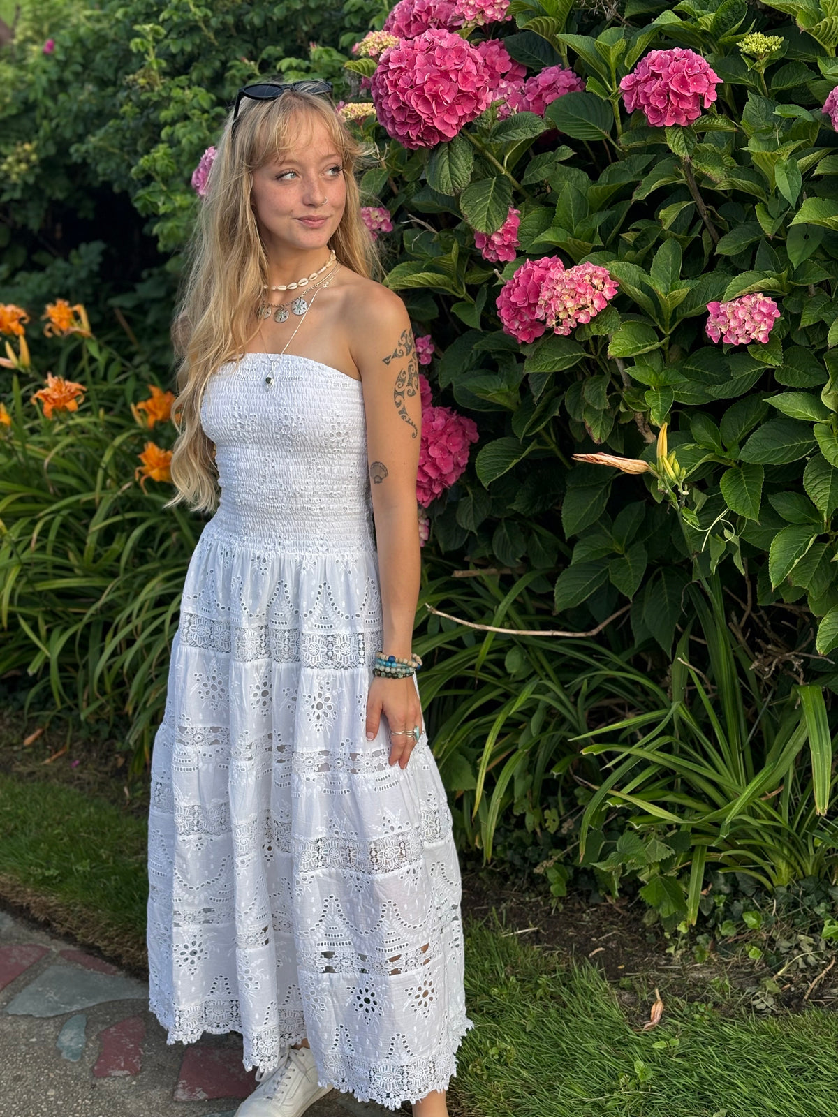Woman in a strapless white eyelet dress standing in front of pink flowers