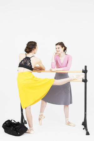 Two ballerinas stretching at the barre, one wearing the Cosette lace back bralette, both wearing the Mireille French midi skirt by Le Mireille Marche.