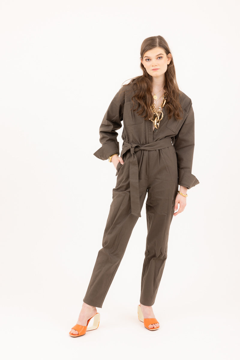 Young woman wearing an olive green jumpsuit styled with a gold chain necklace and orange heels.