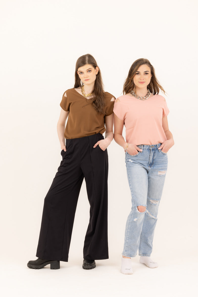 Two women wearing Le Mireille Marche tops, one in brown paired with black wide-leg pants, and the other in pink with ripped jeans, both accessorized with statement necklaces.