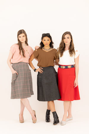 Three women modeling Le Mireille Marche skirts and tops, featuring a pink Julie top with a pink plaid skirt, a brown Julie top with a dark denim skirt, and a white Julie top with a red midi skirt.