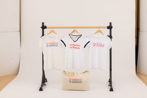 Graphic logo tee shirts and a canvas tote bag with the french sayings "le weekend", "oui, oui" and "Très Sportive Très Élégante" hanging on a ballet barre.