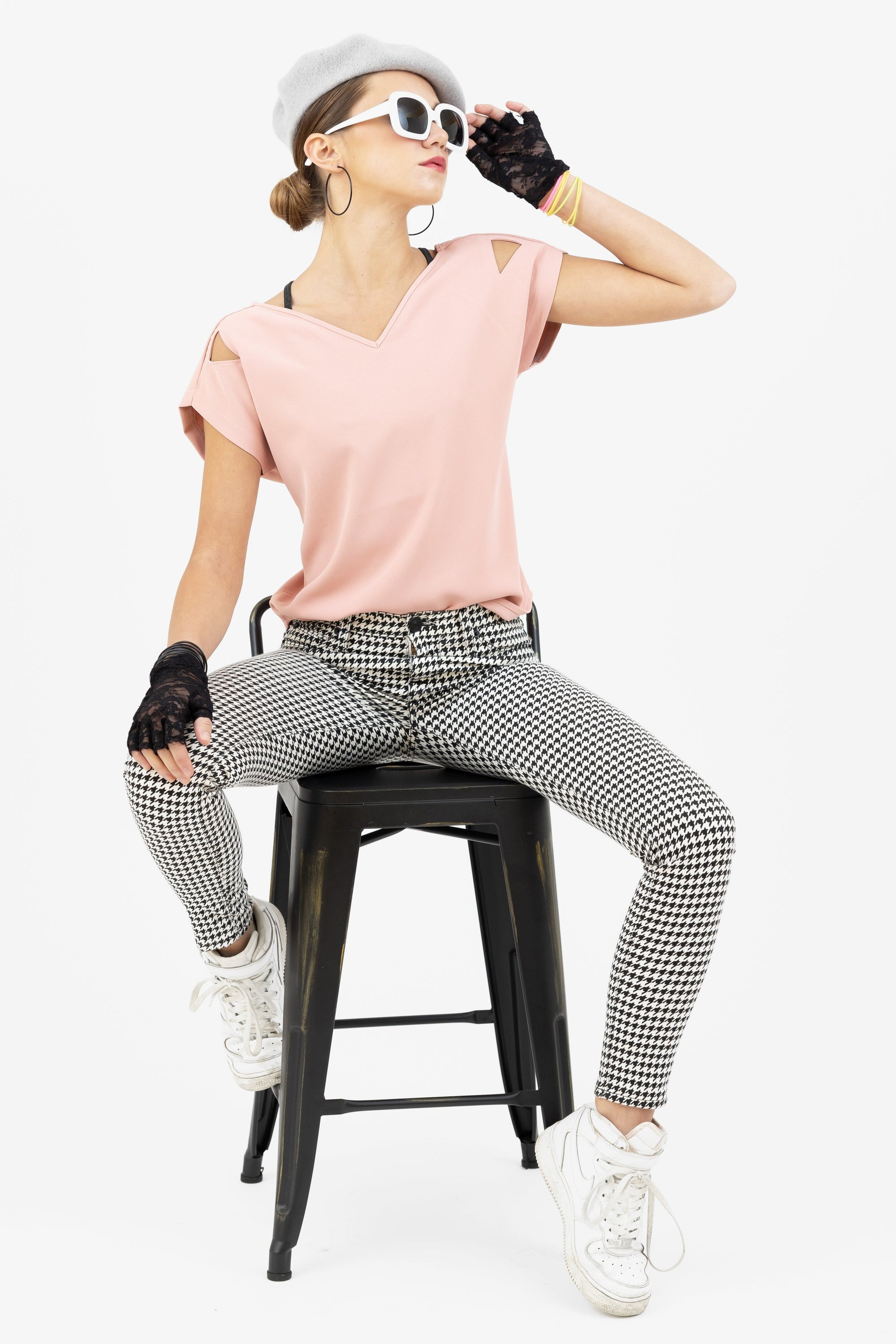 Woman in a pink Julie top and houndstooth pants from Le Mireille Marche, sitting on a stool, wearing a beret, sunglasses, and lace gloves.