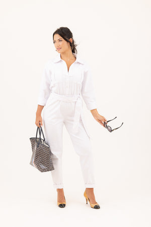 Stylish woman with her brunette hair effortlessly pulled back in a ponytail wearing the Madeline jumpsuit in white, paired with two tone pumps and a designer tote.