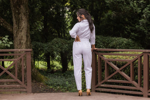 The back view of the jumpsuit in white, worn by a stylish woman with dark hair and heels.