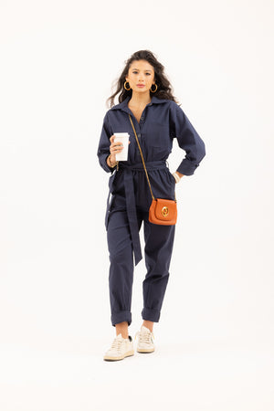 Woman wearing a navy jumpsuit from Le Mireille Marche, accessorized with an orange Gucci crossbody bag, Golden Goose trainers and holding a Starbucks coffee cup.