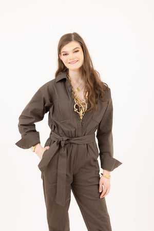 Woman in an olive jumpsuit from Le Mireille Marche, styled with layered gold necklaces and bracelets.