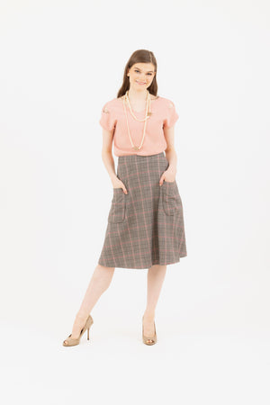 A woman wearing a pink Julie top and rose tartan plaid skirt from Le Mireille Marche, accessorized with a pearl necklace and beige heels. Paris fashion week.