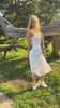 Girl dancing in a white eyelet strapless midi dress in a park.