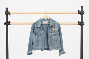 Le Mireille Marche denim Jean jacket adorned with vintage enamel pins, hanging on a ballet barre.