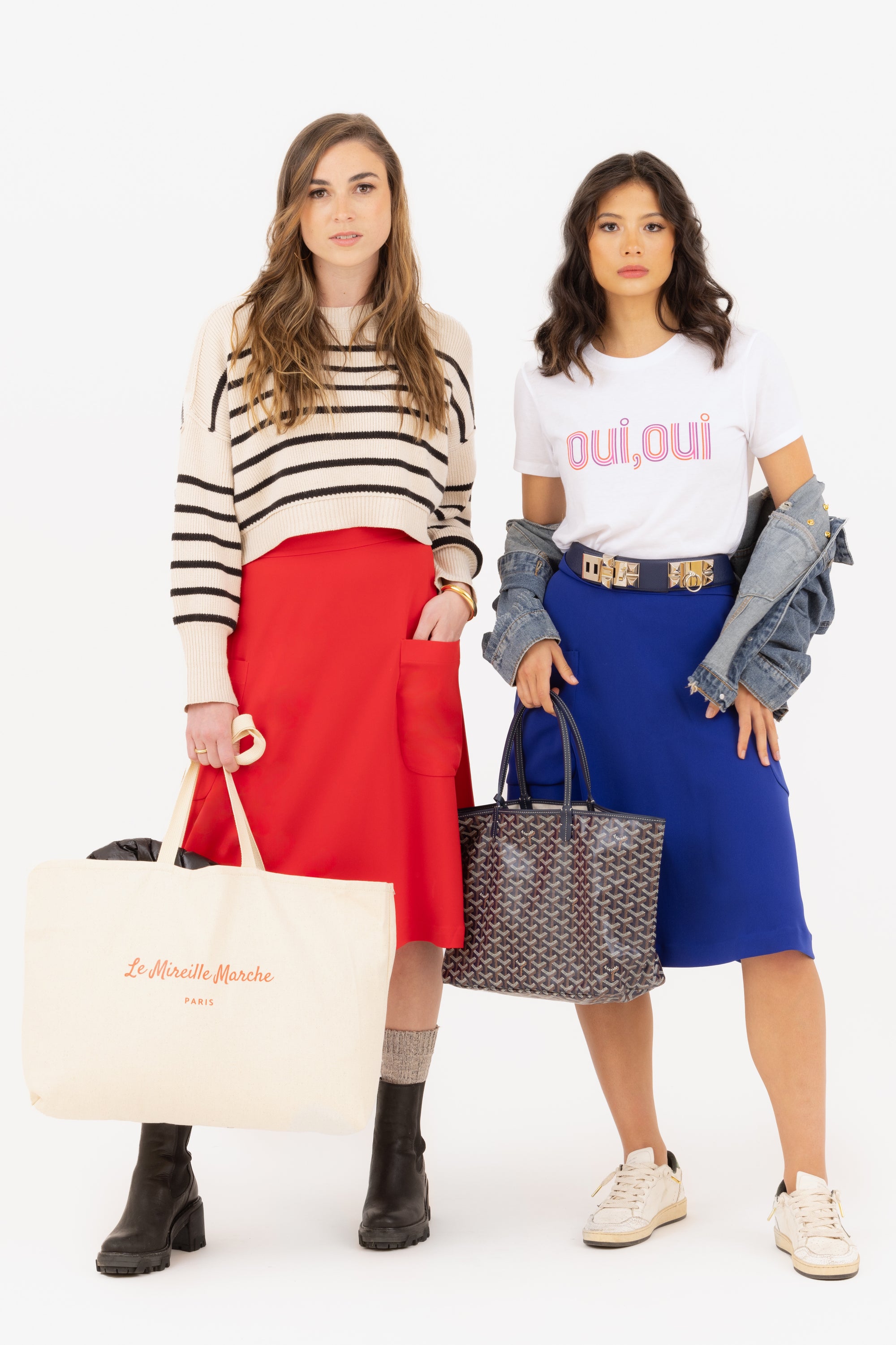 Chic, raven haired woman in oui oui graphic tee, jean racket and Mireille two pocket midi skirt in blue shopping  with her friend, who is wearing Mireille two pocket midi skirt in rouge/red.