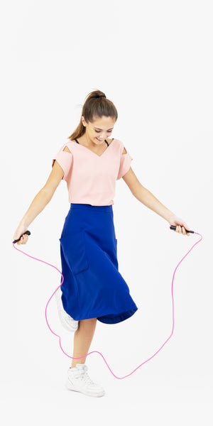 Young French woman in Julie double V top in rose/pink and Mireille two pocket midi skirt in electric blue  joyfully skipping rope.